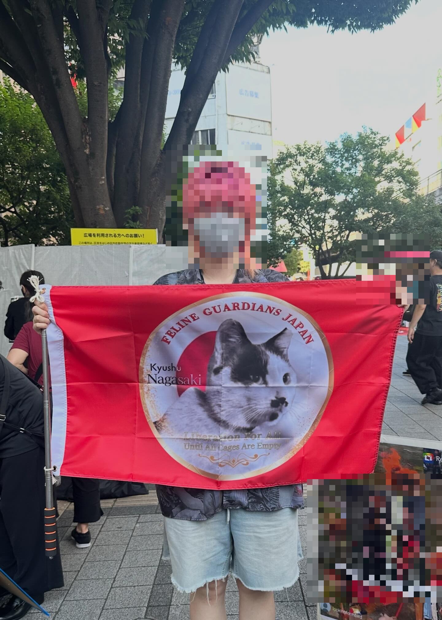 Eine unterstützende Person hält im Freien ein rotes Banner mit Tierdarstellungen; das Gesicht und ein Bereich des Originalbildes, der ein Kind zeigen könnte, wurden in der öffentlichen Fassung verdeckt.